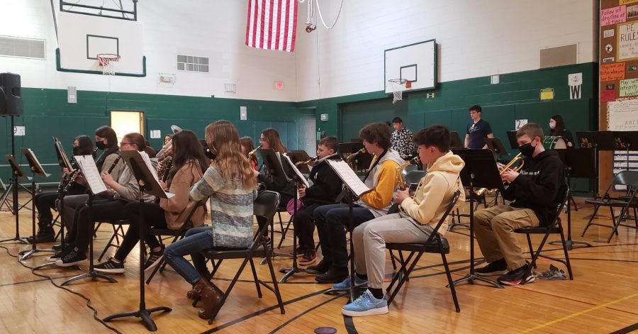 students sitting on chairs in gym playing instruments