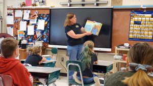 teacher reads book to students in front of a chalkboard