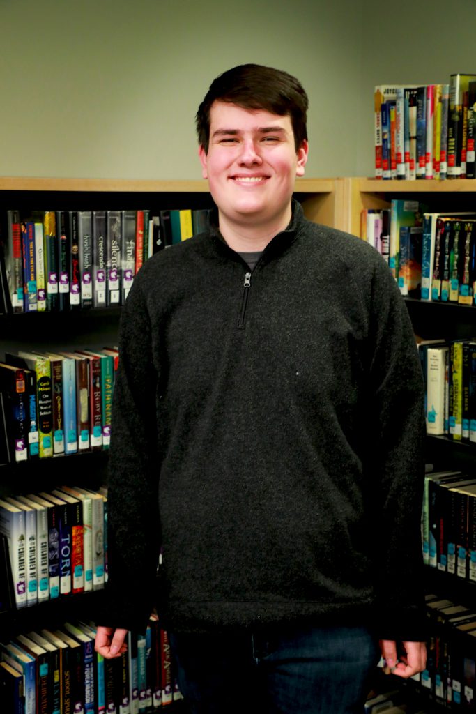tall student towering over bookcase in library