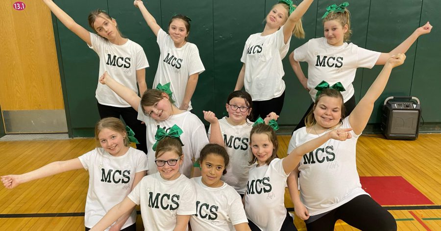 11 students wearing white shirts with MCS on it pose with arms out cheerleader-style
