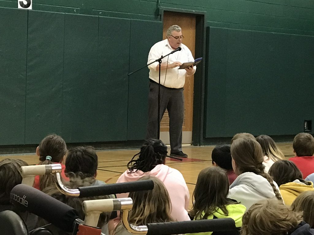 author reads to students sitting on gym floor 