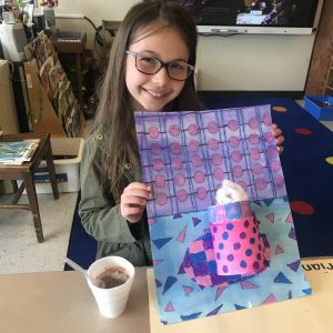 student holds up art project of a mug with hot cocoa 