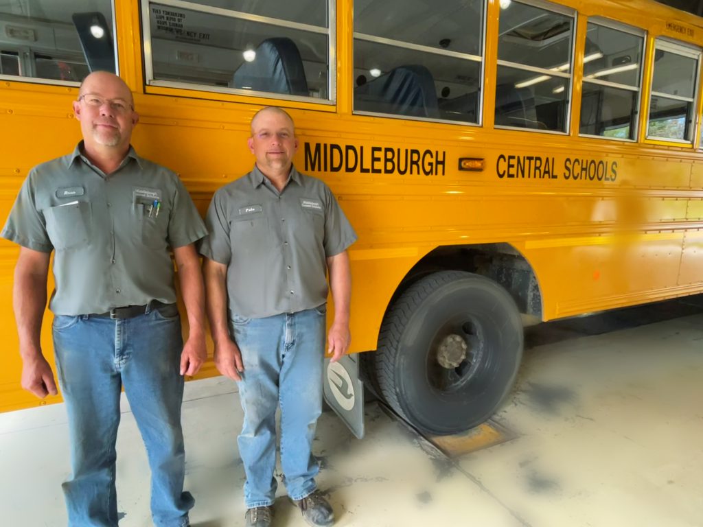 two mechanics standing in front of a bus