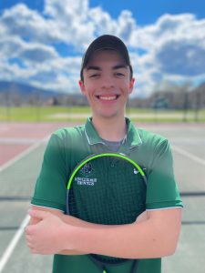 student standing on tennis courts holding a racket close to his chest