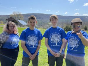 four students standing in a row all wearing the same blue T-shirt with a white tree on it 