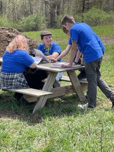 two students sitting at picnic table with two others standing over them 