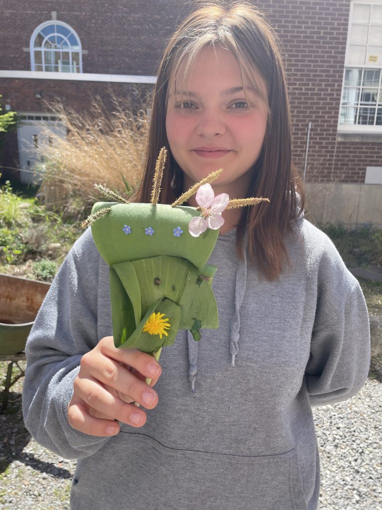 students standing outside holding a leaf with flowers and other plant-like things