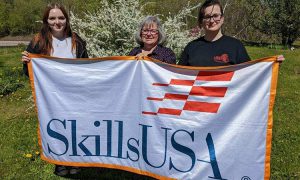 three people hold up a SkillsUSA banner at a park