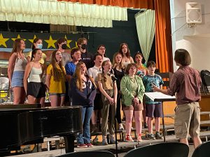 student choir singing on stage and being directed by their teacher