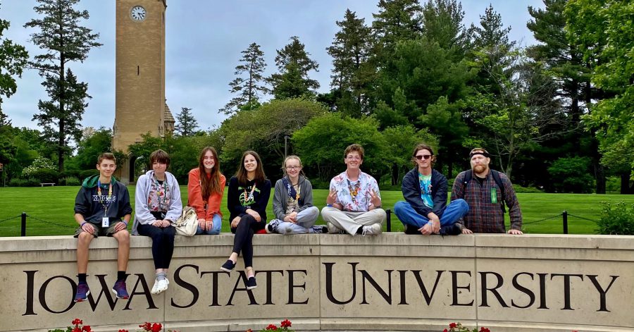 seven students sitting on a sign for Iowa State University and their coach is standing behind the sign