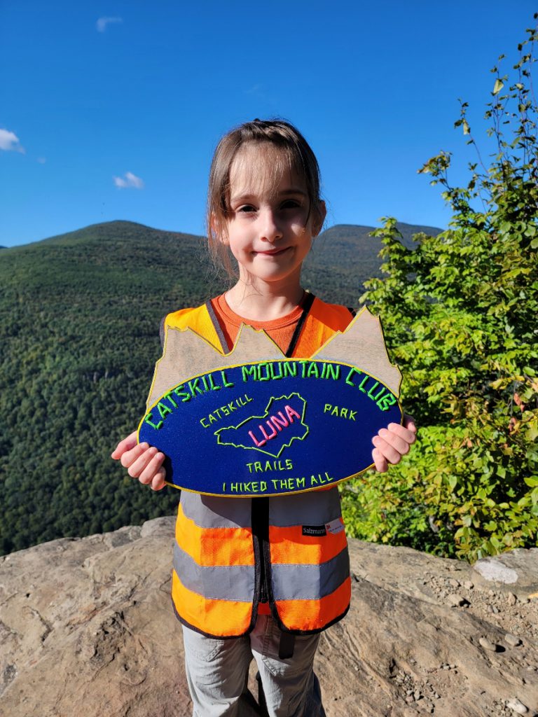 young child on top of a summit she climbed holding a custom sign made by her dad