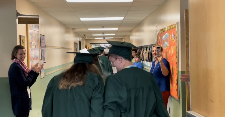 students and teachers line hallway to cheer on graduates in caps and gowns