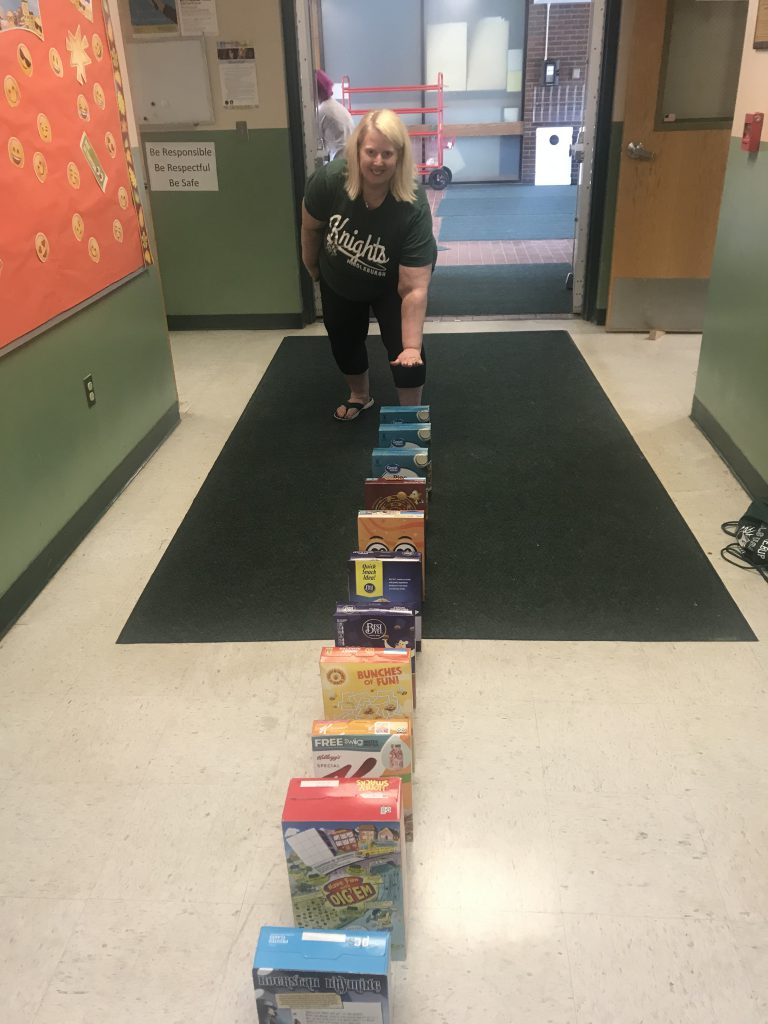 woman crouches down with one hand on a box of cereal ready to topple them over like dominos 