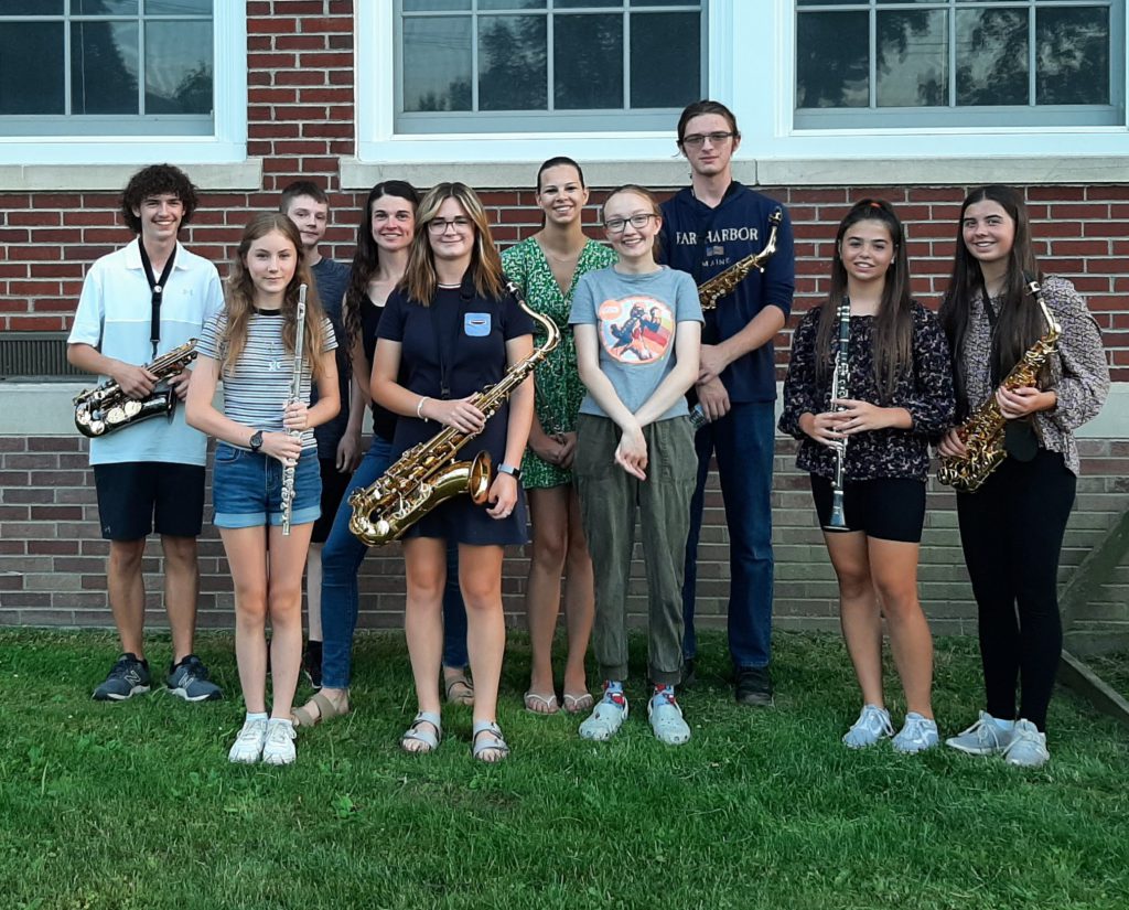 ten people standing with their instruments in front of a brick school with big windows above them