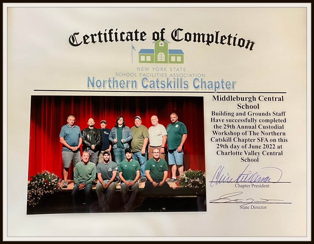 certificate of completion with a picture of seven staff members standing in front of a red curtain and four staff sitting on the stage