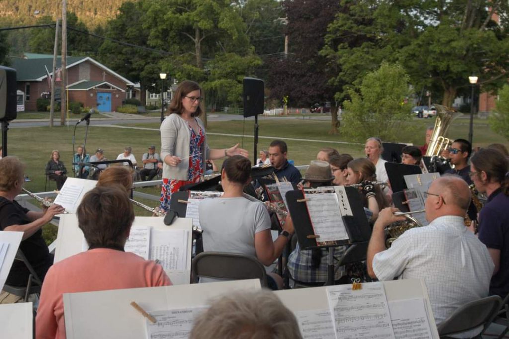 music conductor stands before people playing instruments 