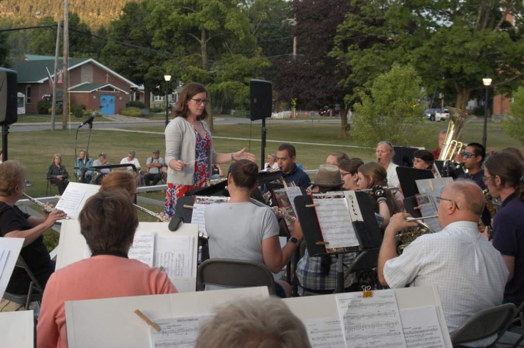 music conductor stands before people playing instruments