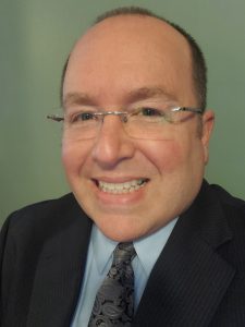 man wearing suit, has glasses and is smiling