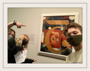 one student looking at camera and two others pointing to artwork