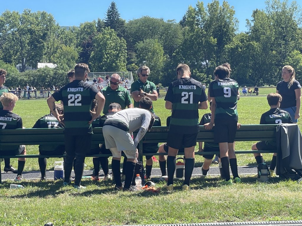 soccer coach talking to team near bench