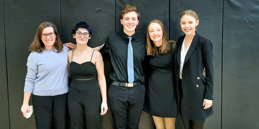 Five students pose against a dark background. They are wearing formal dress