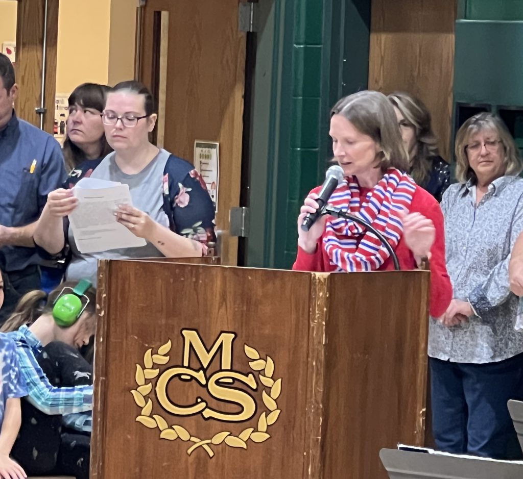 An adult speaks from behind a podium labeled with the Middleburgh crest