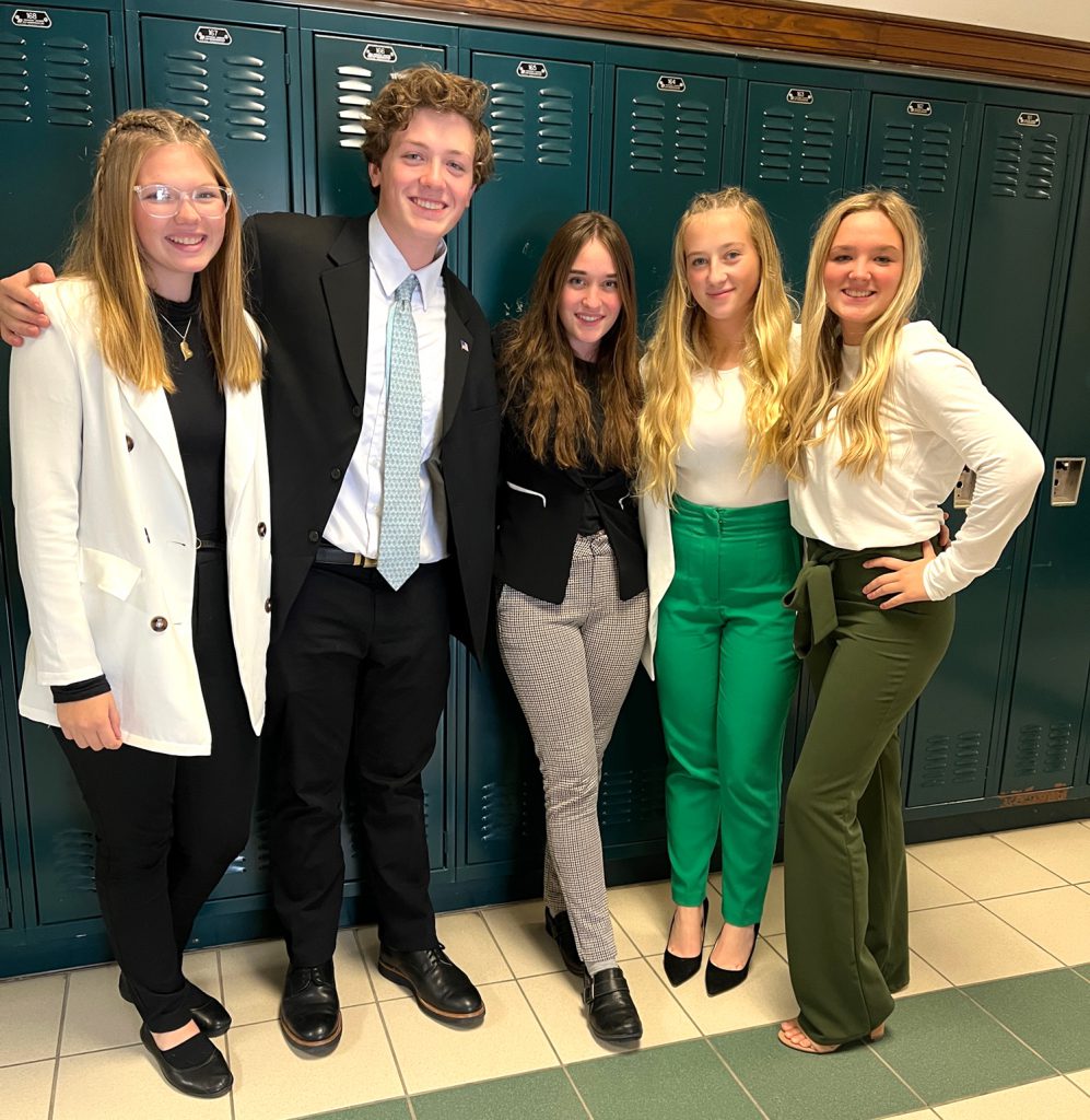 Five students stand in a school hallway wearing professional dress