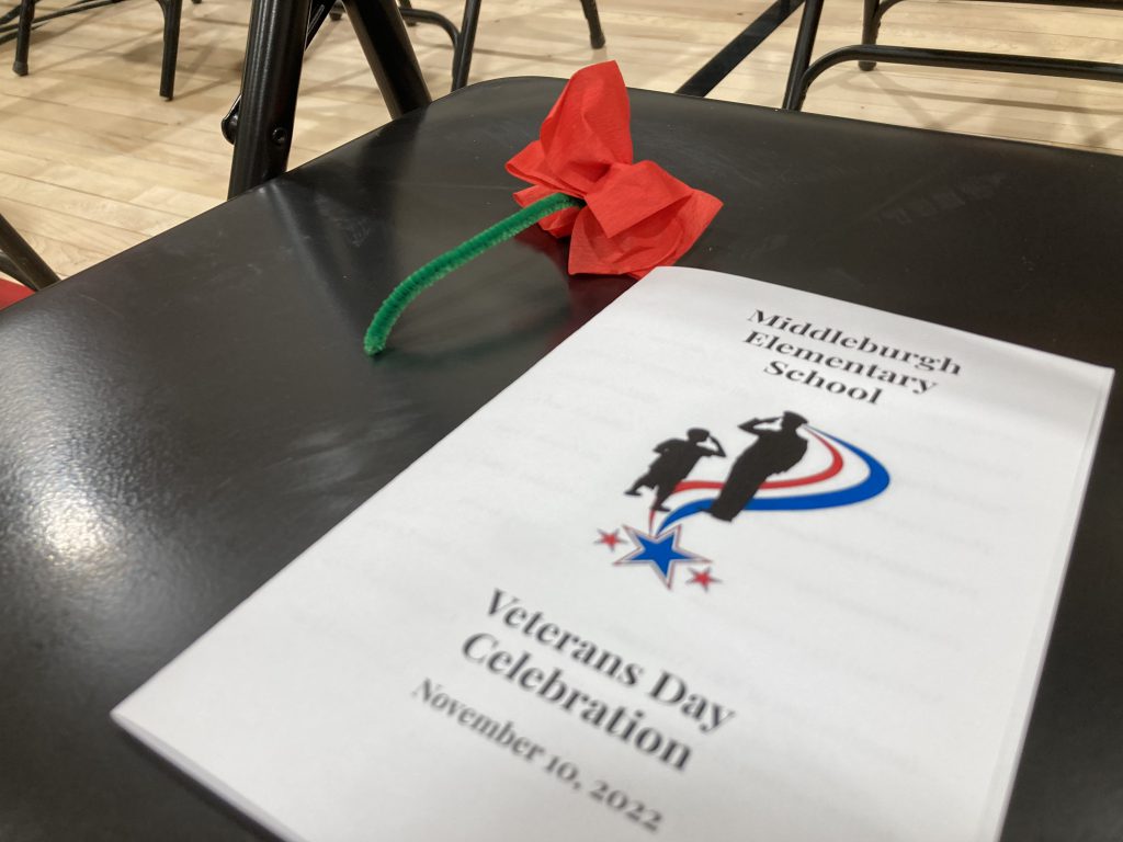 A printed program rests on a chair alongside a paper poppy