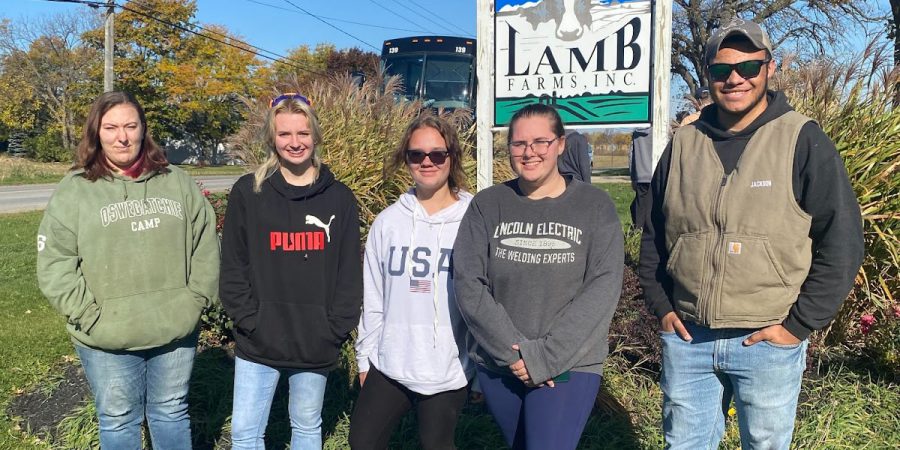 Students stand in front of a sign that reads Lamb Farms