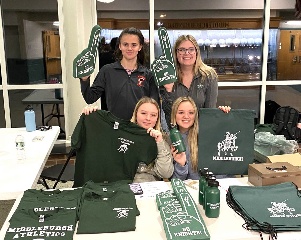 Four students pose at a table showcasing MCS athletics gear