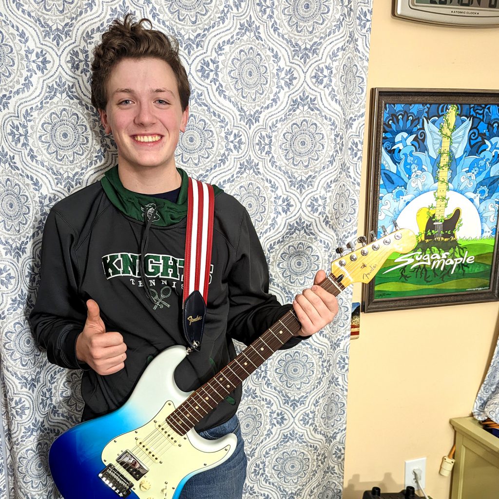 A student gives a thumbs-up while holding an electric guitar