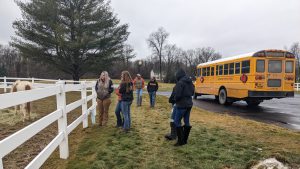 Students in the grades 11-12 Equine Science class visited Windhorse Thoroughbreds LLC and Albany Therapeutic Riding Center (ATRC) on Jan. 6 and met with experts in horse breeding and therapeutic riding. Students stand between school bus and fence where a horse is grazing.
