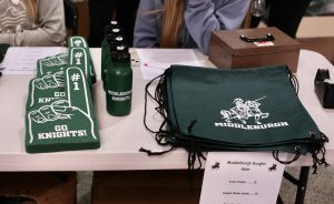 Green Middleburgh water bottles, foam fingers, and backpacks on a table ready for sale.