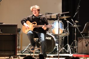 A teen signs and plays guitar.