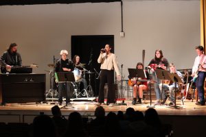 A group of teens singing and playing instruments on stage.