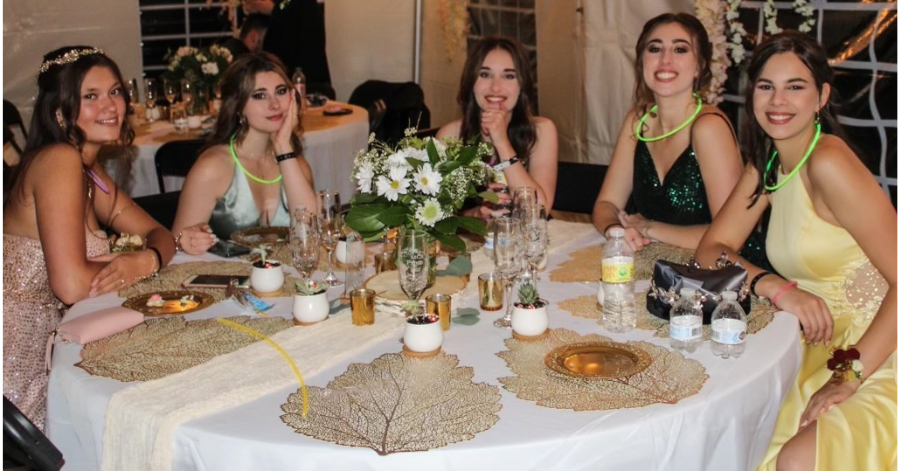 Five teenage girls sit at a table during their prom night.