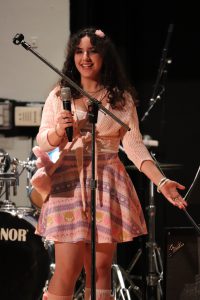 Teen girl holds mic and smiles at audience.