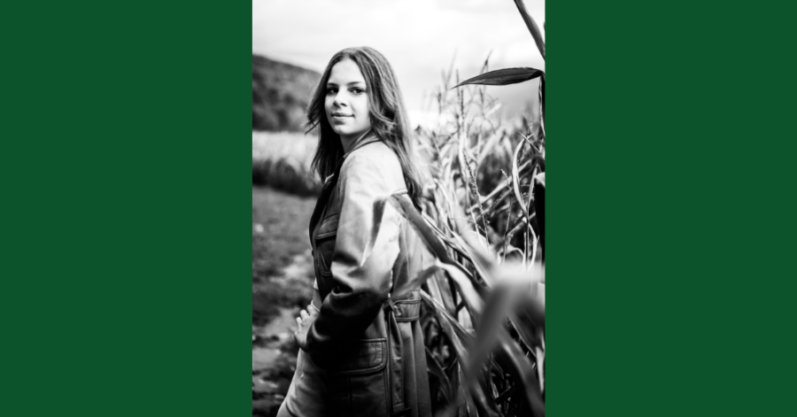 Teenage girl stands in corn field. She is looking over her shoulder .