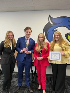 Four high school students wearing business attire smaile at the camera. One is holding a certificate.