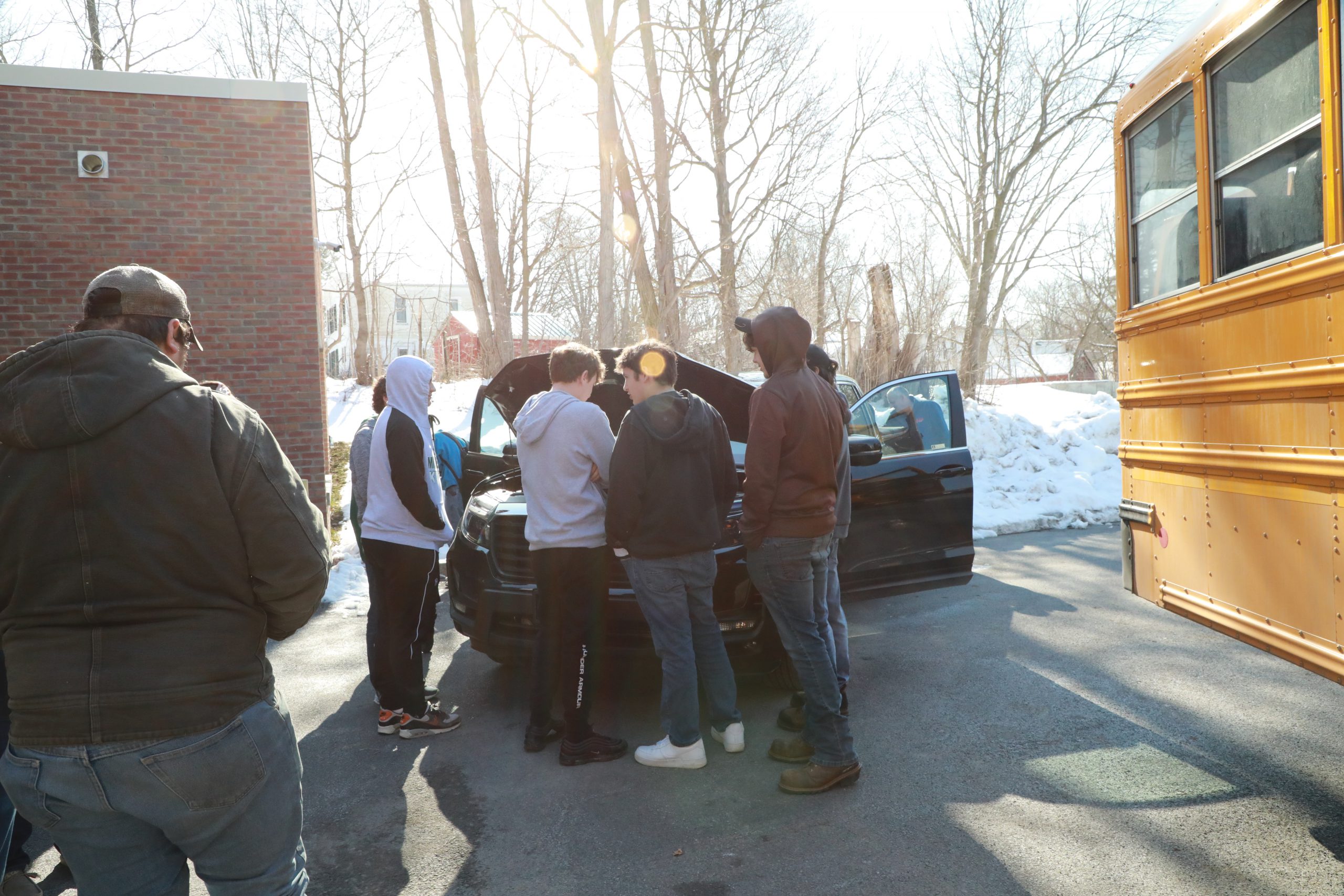 Students gather around a car with an open hood.