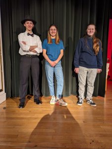 Three characters from "Little Shop of Horrors" stand on stage.