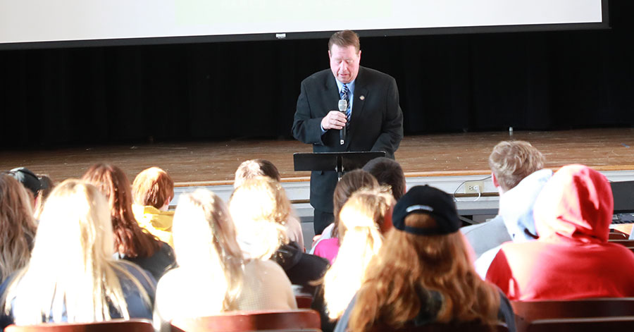 Assemblyman Chris Tague stands in front of stage. Students are looking on.