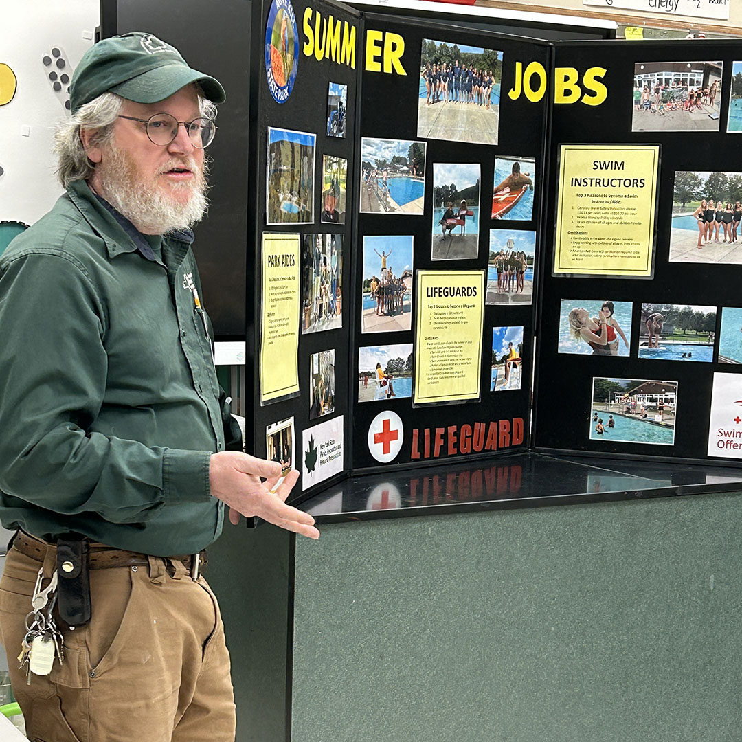 Chris Kenyon NYS Parks, Recreation and Historic Preserves stands in front of bulletin board of summer job openings.