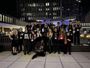 Members of the Modern Band at the Eastern Division Conference. They are standing in front of modern buildings at night. THey are all wearing black.