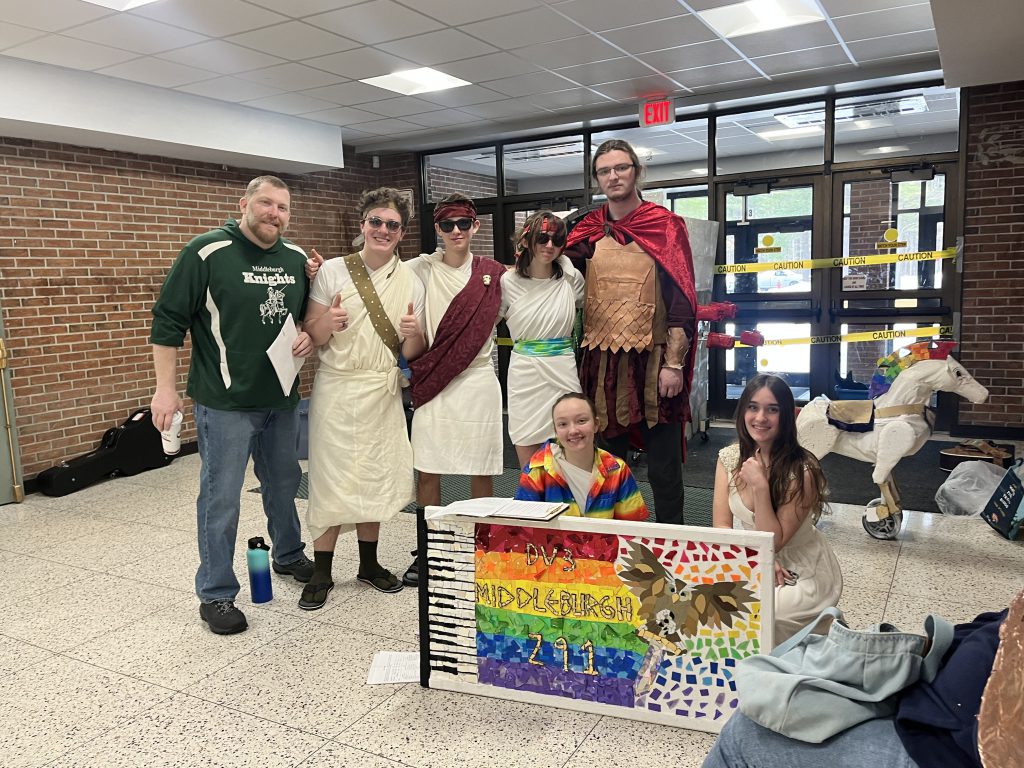 Group of teenagers dressed in togas and capes with their coach.