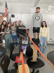 Students stand with parts of a Rube Goldberg machine.