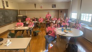 Students wear matching shirts and give a thumbs-up.