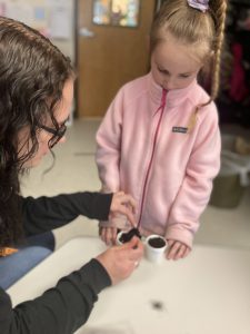 Teen shows child how to plant seeds in a cup.