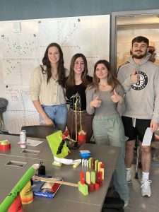 Students stand with parts of a Rube Goldberg machine.