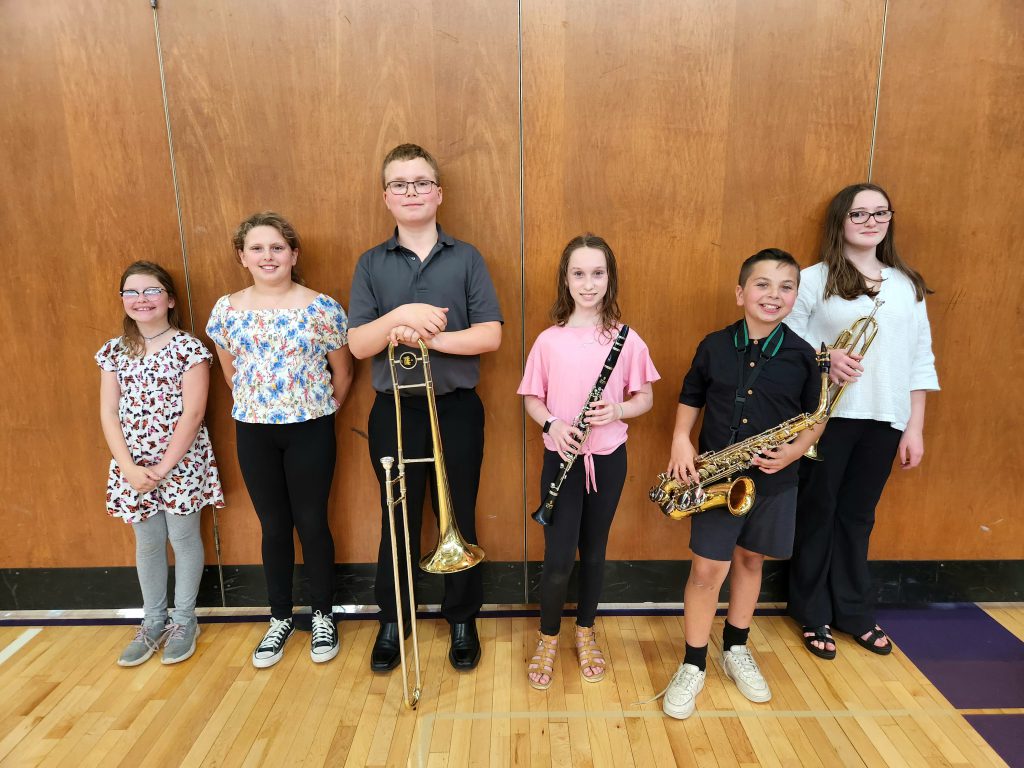 Six students stand together. Four of them are holding musical instruments.